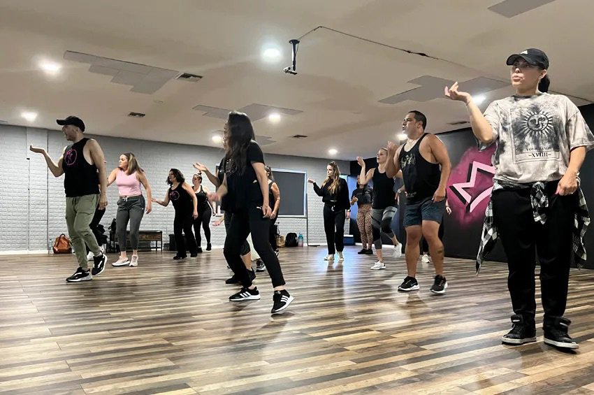 Adult hip hop dance class in session at the Royal Peacock Studio in Oakland Park, Florida, with a group of diverse dancers following choreography in a modern studio setting